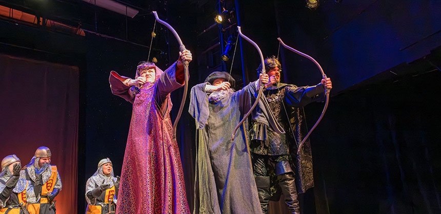 Theatre students on stage in costumes with bows and arrows